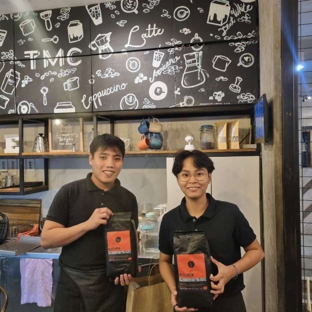 Two café staff behind the counter holding branded bags from their coffee bean supplier